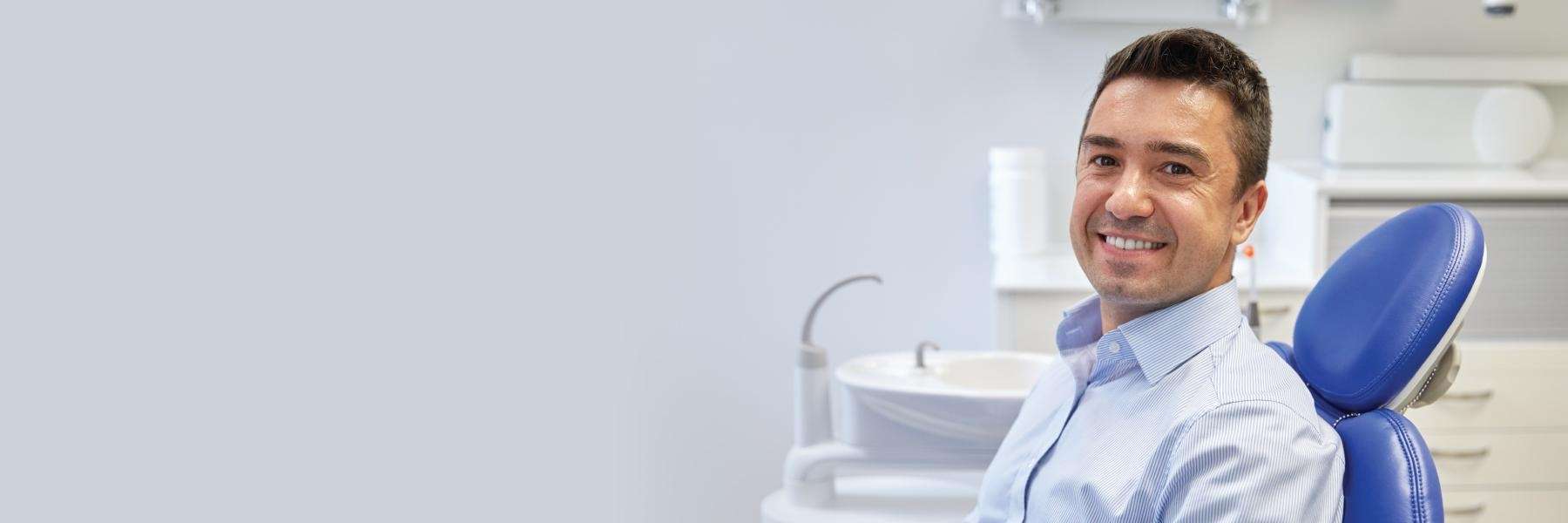 A smiling man sitting in a blue dental chair in New Orleans