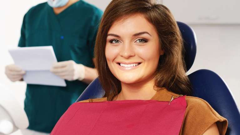 Smiling woman sitting in a dental chair wearing a protective bib.